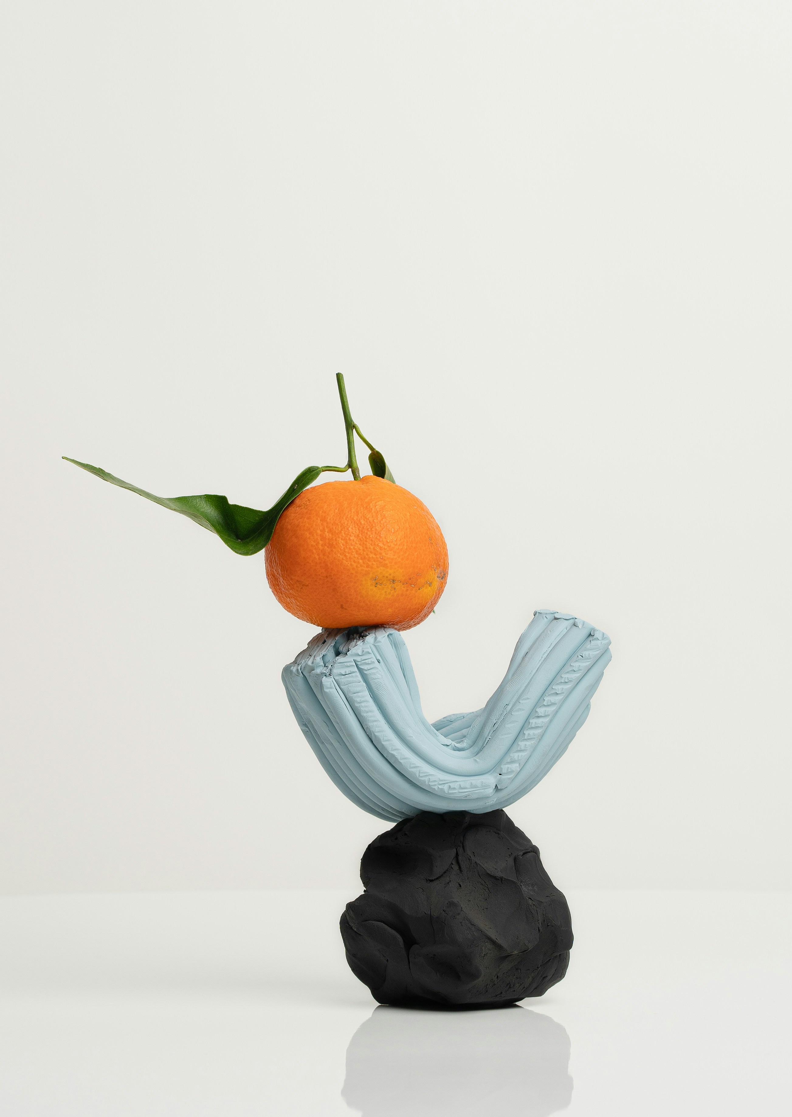 A handmade towerlike sculpture. A lightblue U-shaped piece sits on a roughly carved black base and has an orange balancing on top.